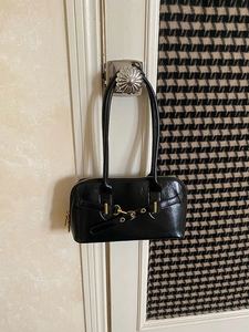 Detailed view of a black leather bowling bag with gold hardware hanging on a door handle