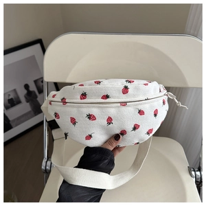 Detail of strawberry printed corduroy crossbody bag texture and adjustable strap on a chair
