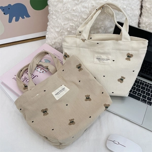 Corduroy tote bags with bear embroidery in khaki and cream, set on an office desk