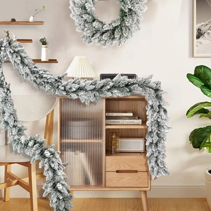 Detailed view of snowy Christmas wreath and garland set on a wooden cabinet