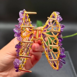 Detail of a golden butterfly hair claw clip with purple amethyst crystals held by hand