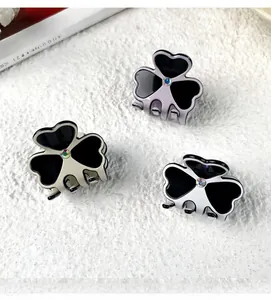 Close-up of three small clover hair clips with glossy black inlay and rhinestone center