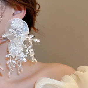Vue macro de boucles d'oreilles en dentelle blanche avec broderie florale et texture mesh