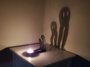 Close-up of metal silhouette candle holder casting a spooky human shadow on a wall
