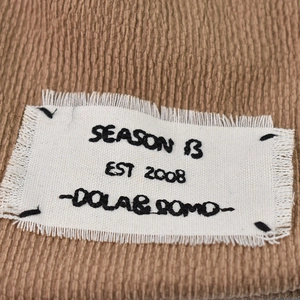 Close-up of brown corduroy hat detail featuring a vintage frayed canvas logo patch