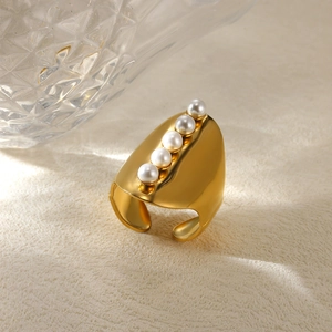 Detail of a wide gold ring featuring five gradient white pearls on a textured surface