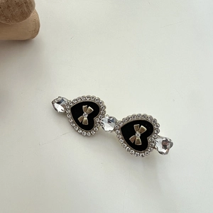 Macro detail of rhinestone hair clip featuring black heart charms and gold bows