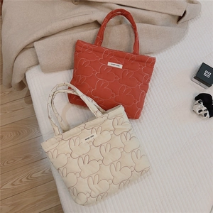 Close-up of rabbit embroidery and quilted texture on red and beige tote bags