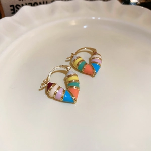 Macro shot of colorful enamel heart earrings with gold trim on white porcelain tray