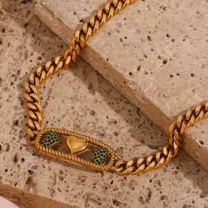 Détail macro de trois breloques cœurs dorés sur une chaîne cubaine avec zircon vert serti