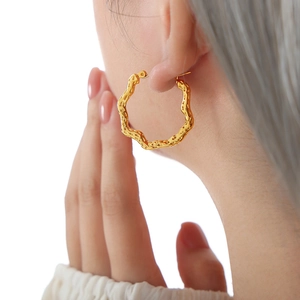 Golden irregular wave hoop earrings with hammered texture on female model ear