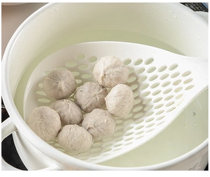 Close-up of a large white heat-resistant strainer scooping meatballs from a pot