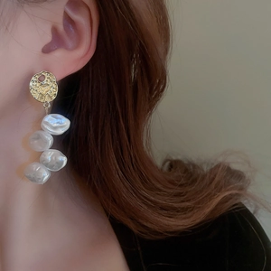 Detail of long drop earrings featuring gold textured metal and four baroque pearls on a model