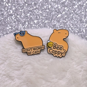 Detail of two capybara enamel pins with Don't Worry Be Capy and Bee Cappy text