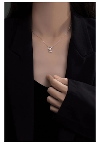 Close-up of silver letter L necklace with dancing zircon on black suit background