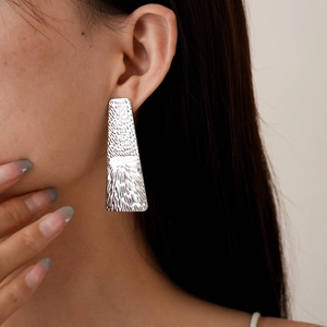 Close-up of geometric silver trapezoid earrings with hammered texture and sunburst engraving