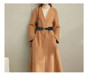 Detail of a wide black elastic waist belt with a golden circular buckle on a wool coat