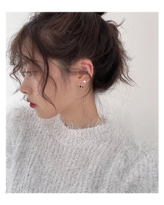 Close-up of star stud earring and black heart pendant on model wearing white fuzzy sweater