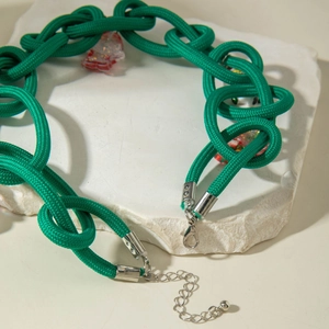 Detail of green woven rope necklace with braided knot texture and resin charms