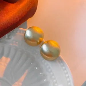 Minimalist matte gold spherical stud earrings displayed on a white textured ceramic plate