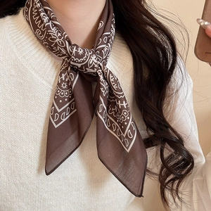 Detail of dark brown silk scarf with white paisley pattern knotted on a white sweater