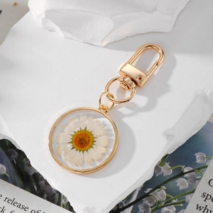 Macro view of golden resin keychain with real white daisy flower detail on white stone