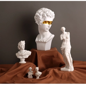Artistic group of white resin Greek sculptures with gold details on brown fabric