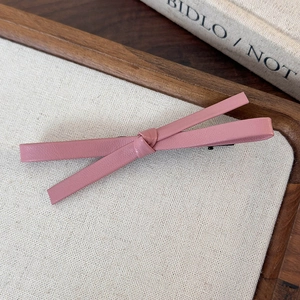 Close-up of pink leather bow hair clip on a wooden tray with a minimalist aesthetic