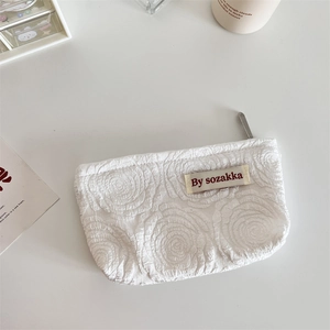 Detail of white makeup bag with embossed 3D rose pattern and metal zipper on top