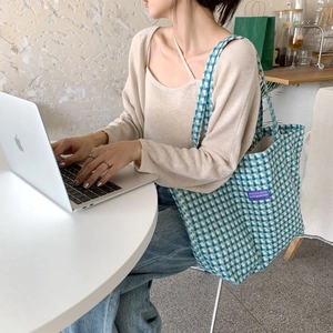 Detailed close-up of a blue and white checkered plaid tote bag used in a cafe setting