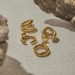 Dettaglio di orecchini a clip dorati con perle e design scolpito su superficie in pietra