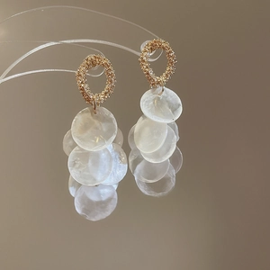 Macro shot of gold circle earrings with white shell pendants and elegant tassel detail