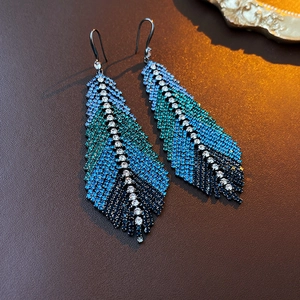 Macro shot of gradient blue feather earrings with crystal inlay on brown texture