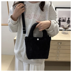 Detail of black corduroy bucket bag worn crossbody with white button and nylon strap