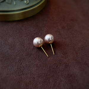 Macro view of elegant pink pearl earrings with gold posts on dark velvet background