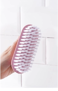 Macro detail of dense white bristles on a pink handheld multi-purpose laundry brush