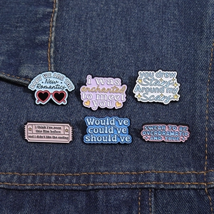 Close-up of six colorful enamel pins with artistic lyrics on blue denim fabric