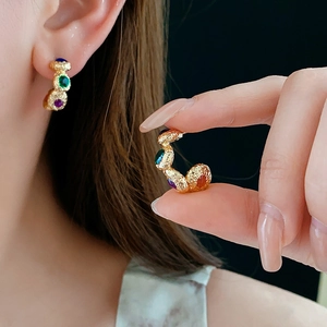 Detail of vintage C-shaped gold earrings with colorful enamel stones on model