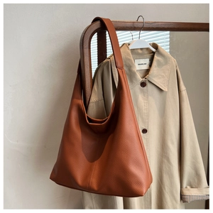 Detail of a large brown leather tote bag with a soft slouchy design hanging on a rack
