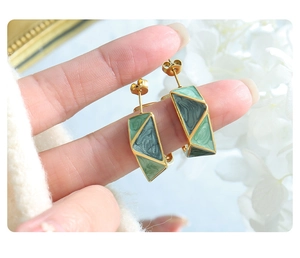 Detail of hand-held geometric gold hoop earrings with green marble enamel inlay