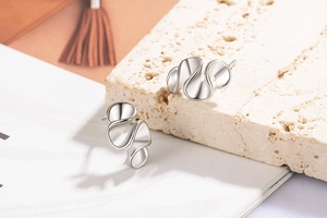 Detail of silver irregular wavy stud earrings on minimalist stone background