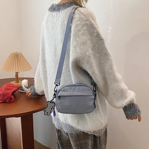 Detail of grey-blue nylon crossbody bag with adjustable strap and checkered bear charm