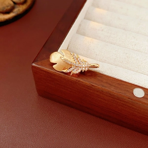 Macro shot of gold feather brooch with micro-pave zircons on a wooden jewelry box