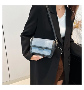 Detail view of light blue denim fabric texture with black leather trim on a shoulder bag