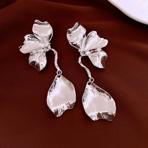 Gros plan de boucles d'oreilles fleurs argentées martelées sur fond de satin foncé