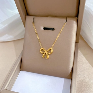 Detail shot of a gold bow pendant necklace resting in a beige premium jewelry gift box