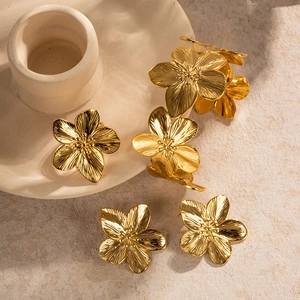 Golden flower earrings set with brushed metal texture on a ceramic tray display