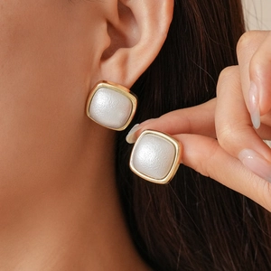 Detailed close-up of golden square stud earrings with white matte inlay on ear