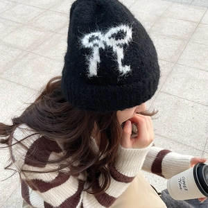 Detail of black fuzzy knit beanie featuring a large white bow pattern and long-haired texture