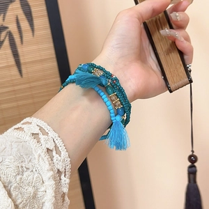 Detail of layered bohemian bead bracelet with blue tassels and golden accents on wrist
